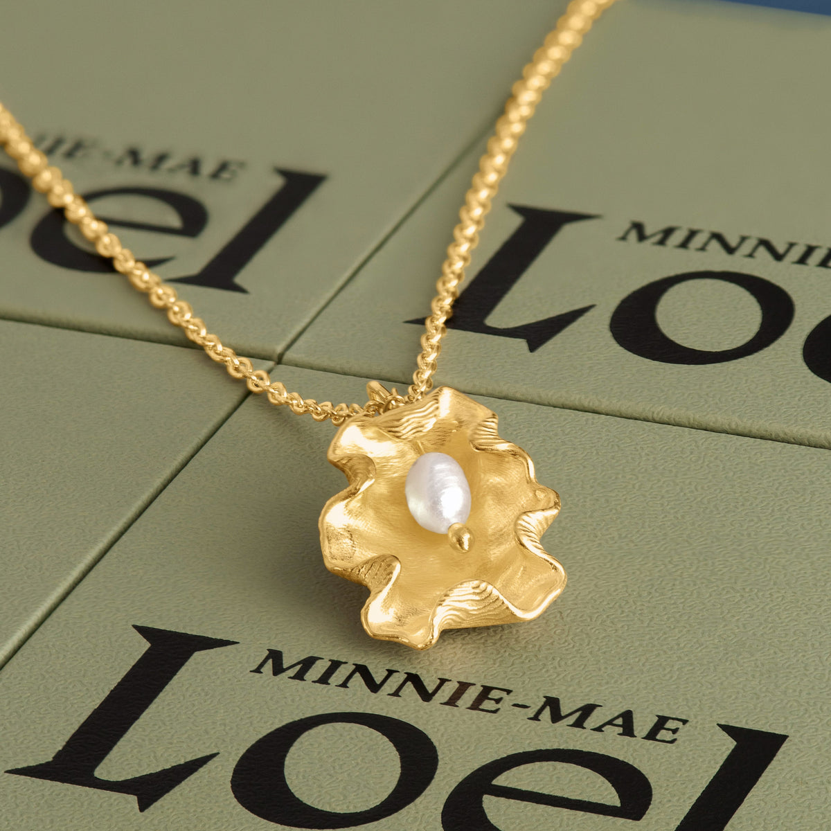 LOEL x Minnie Mae Gold Oyster Shell and Pearl pendant on green boxes flat