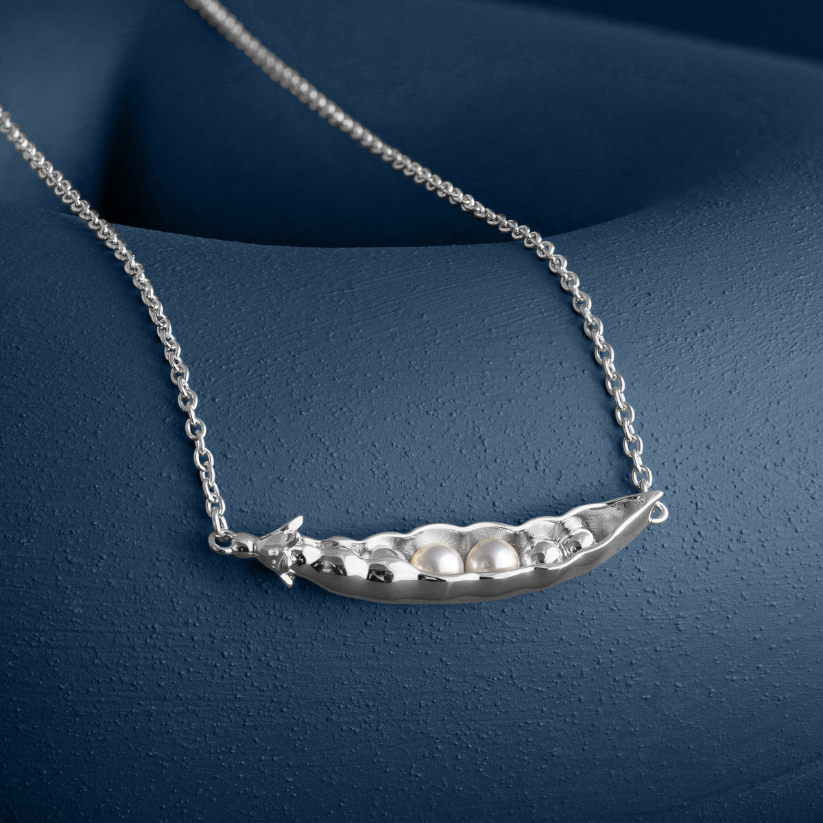 LOEL x Minnie Mae Silver Peas in a Pod Pendant on blue flat lay