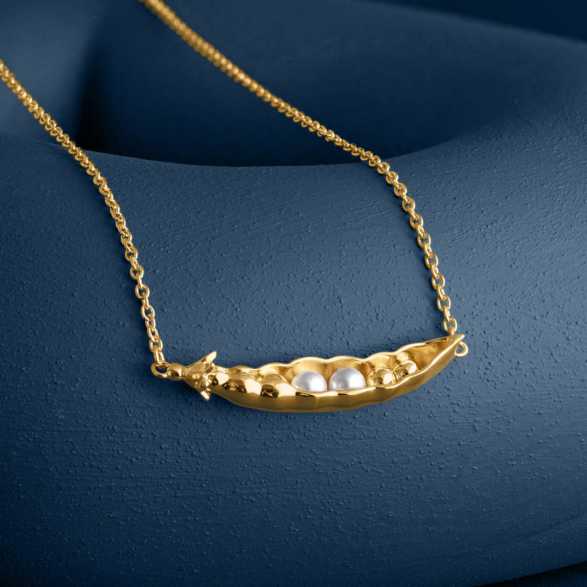 Loel x Minnie Mae Gold Peas in a Pod Pendant on blue flat lay
