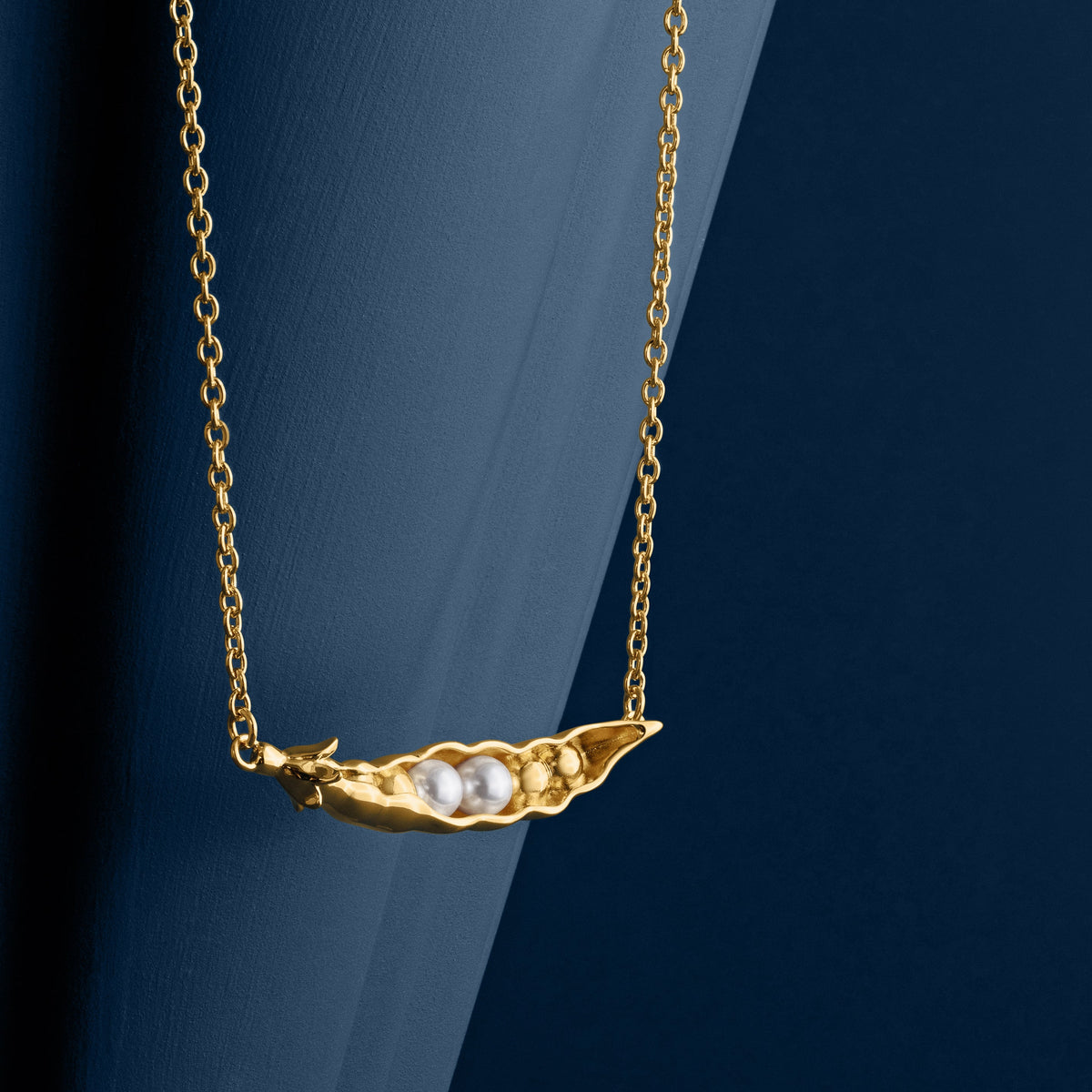 Loel x Minnie Mae Gold Peas in a Pod Pendant hanging on blue