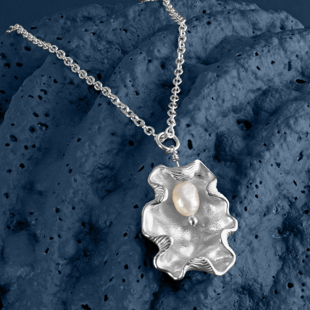 Loel x Minnie Mae Silver Oyster Shell Pendant on blue flat lay