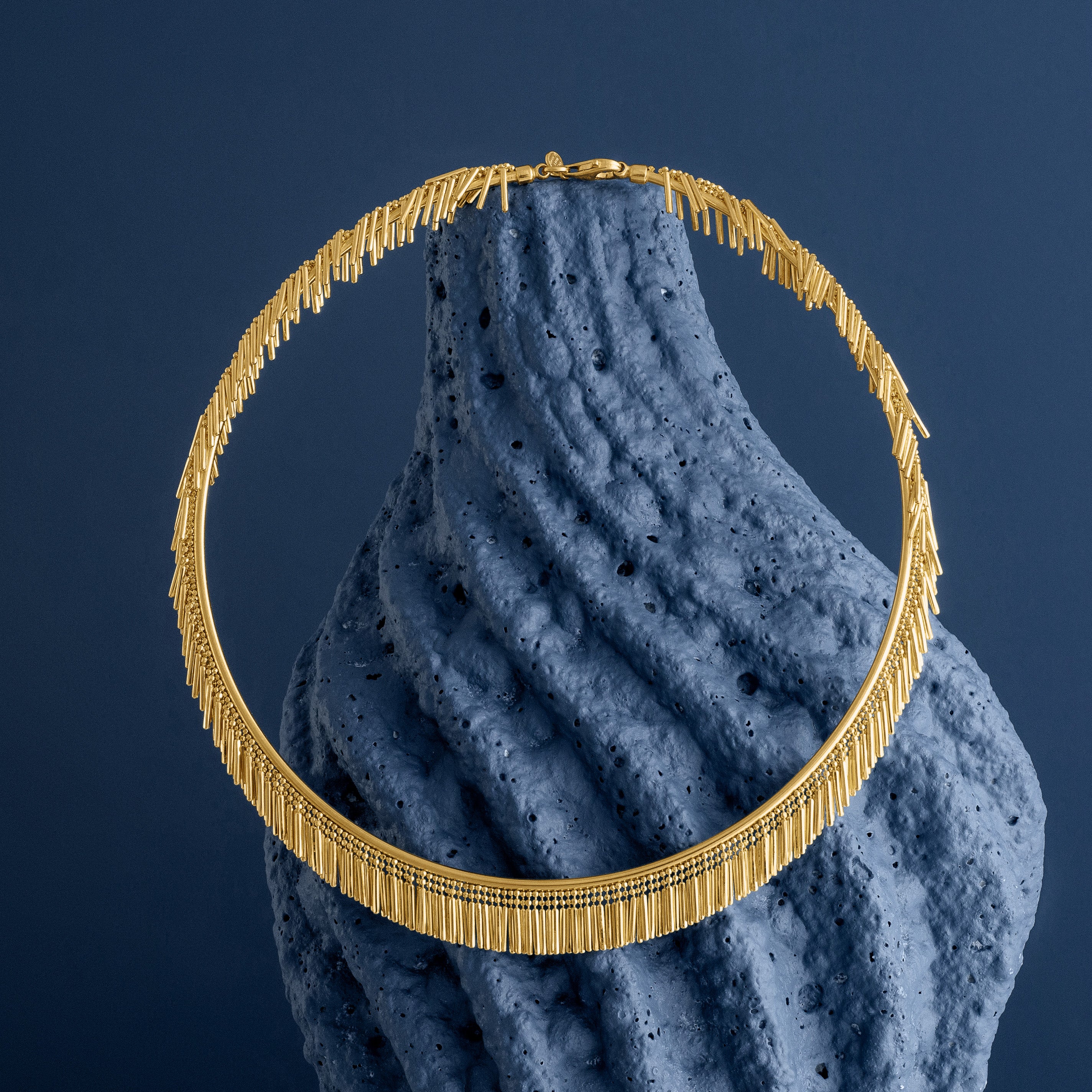 Gold tassel necklace on a textured blue surface with a dark blue background