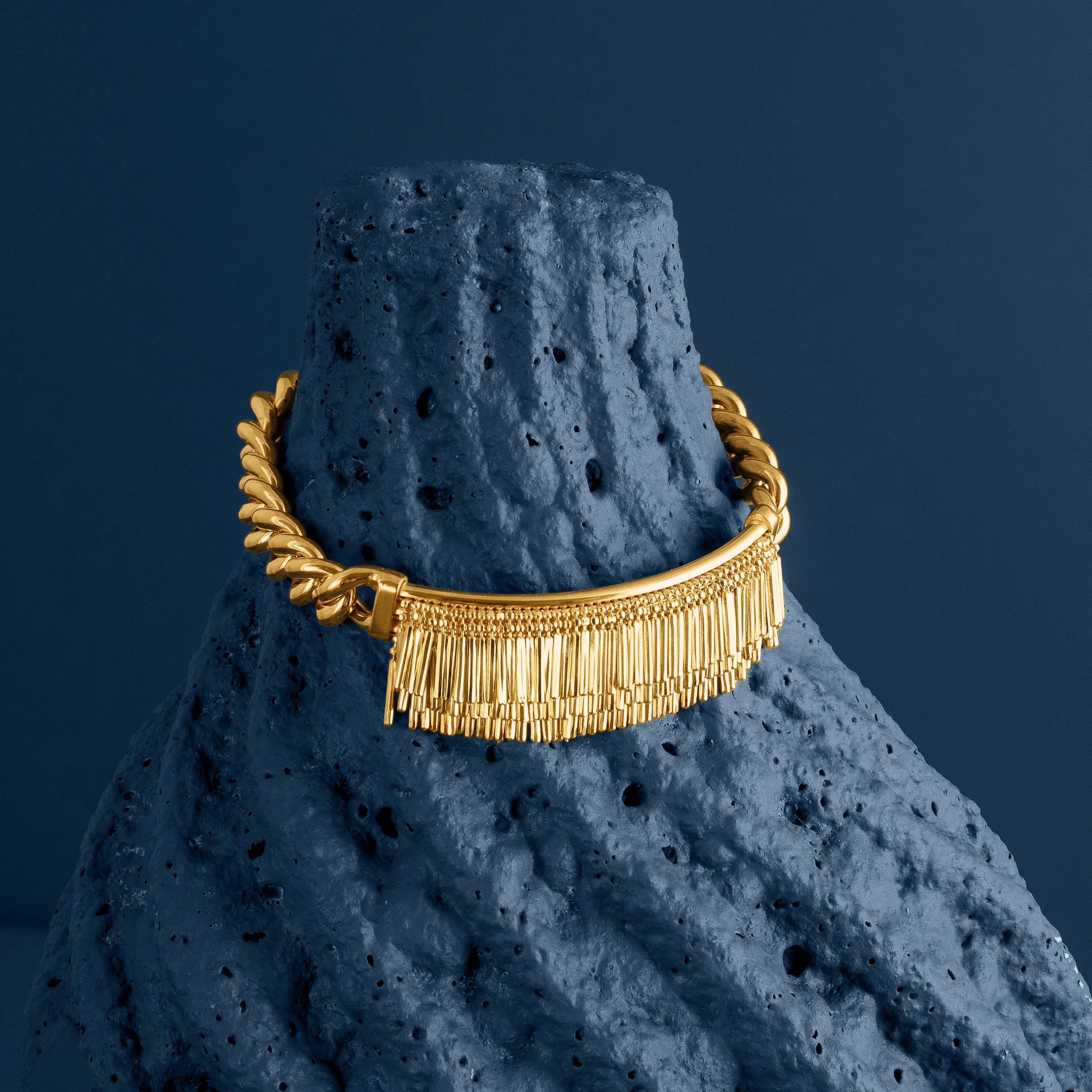 LOEL - Gold tassel and chain cuff bracelet displayed on a dark blue textured stone background