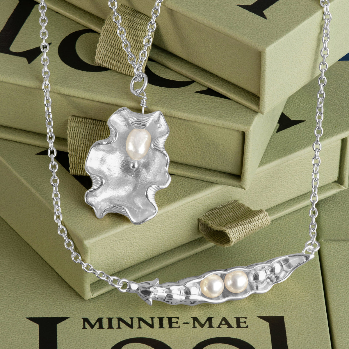 Loel x Minnie Mae Silver Oyster Shell Pendant and Peas in a Pod Pendant on green boxes